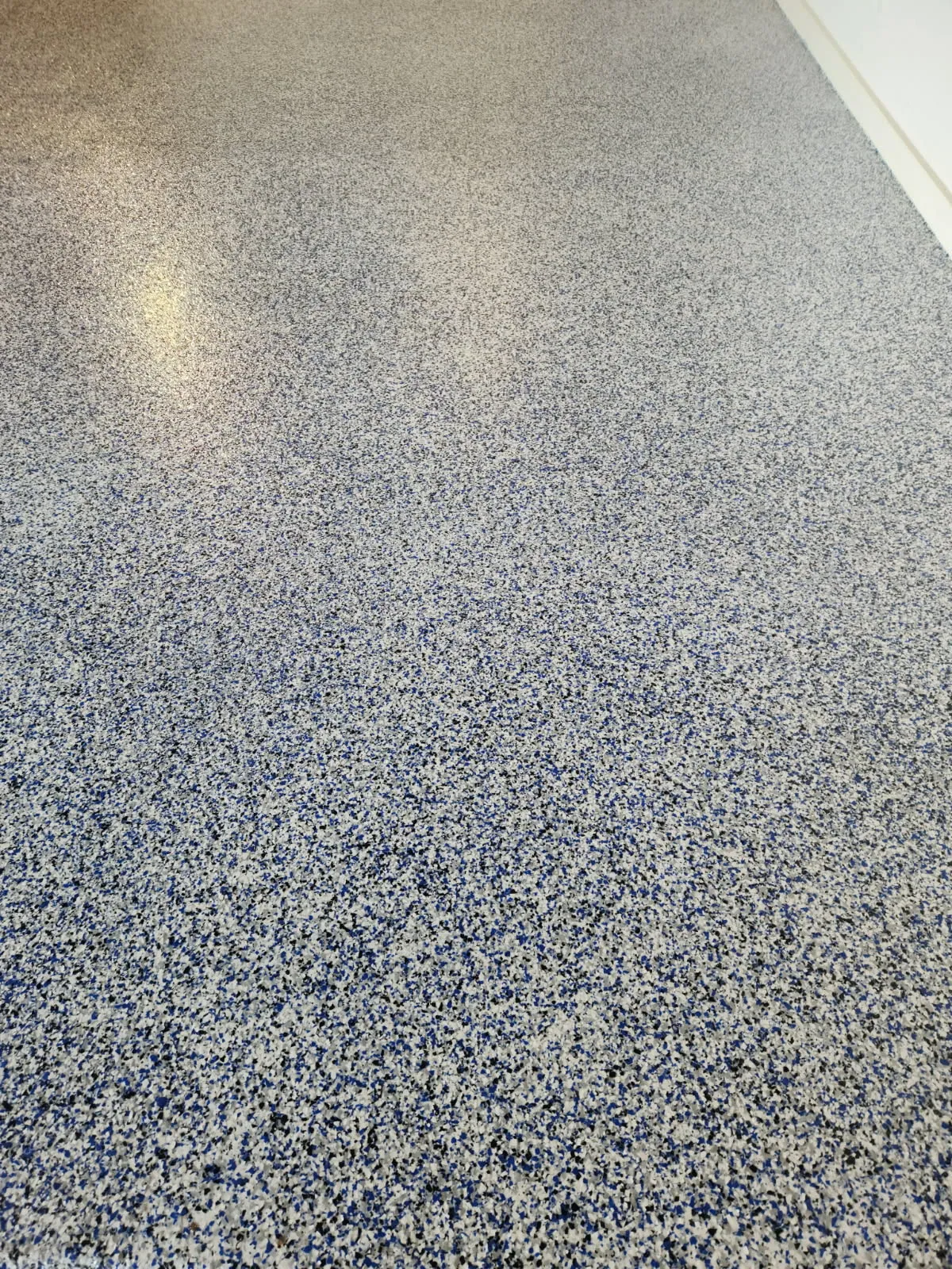Blue flake epoxy floor running to a white wall